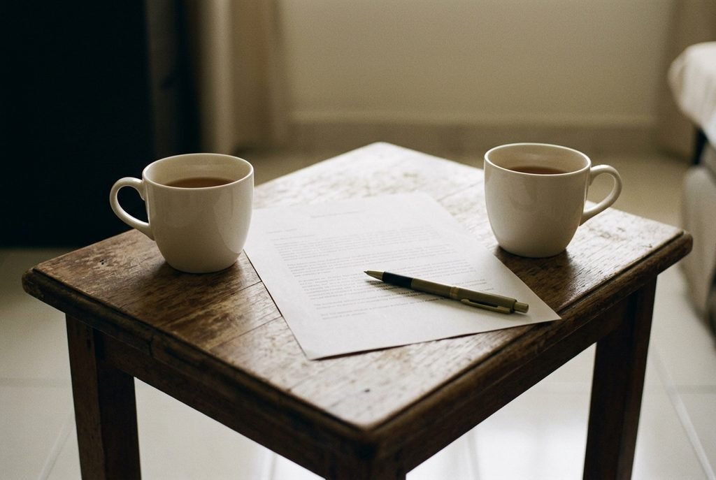 Two cups of tea across a small table with a single sheet of paper and pen between them, suggesting a calm negotiation